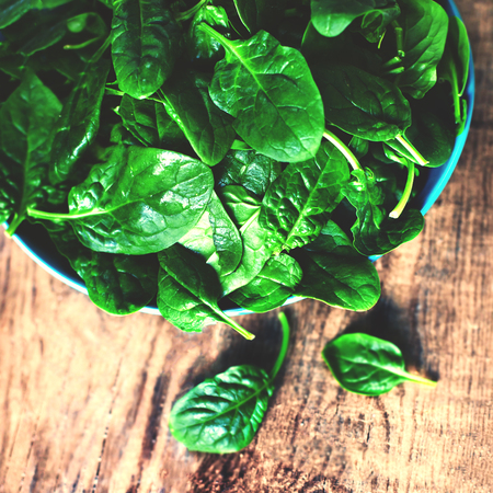 Spinach leaves in a bowl on rustic wooden table close up with copyspace.の写真素材