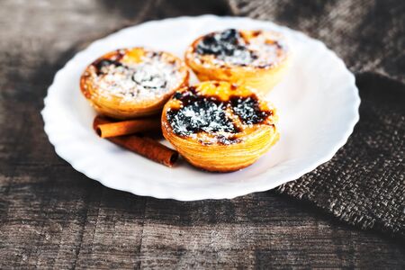 Egg tart  - creamy sweet curstard on white plate on wooden table close up with copy space. Pasteis de Belem dessertの写真素材