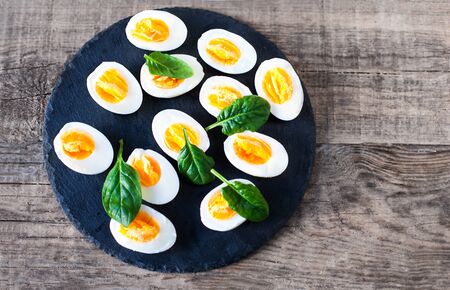 Fresh green spinach baby leaves and boiled eggs cut in a half on wooden background  with copyspaceの写真素材