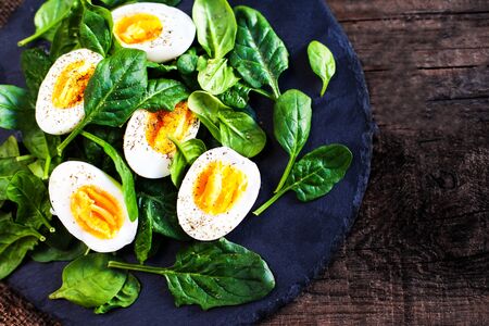 Fresh green spinach baby leaves and boiled eggs cut in a half on wooden background  with copyspaceの写真素材