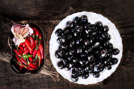 Black olives with red chilli peppers  in a white bowl on wooden table with copy space. Food concept backgroundの写真素材