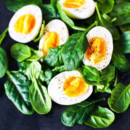  Boiled eggs cut in a half  with Fresh green spinach baby leaves on wooden background with copy spaceの写真素材