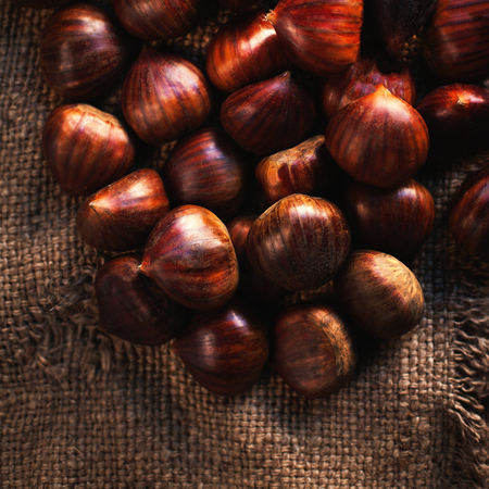 Fresh chestnuts on brown sack bag. Big ripe tasty Chest nuts  on old wooden table with copy space, close up
の写真素材