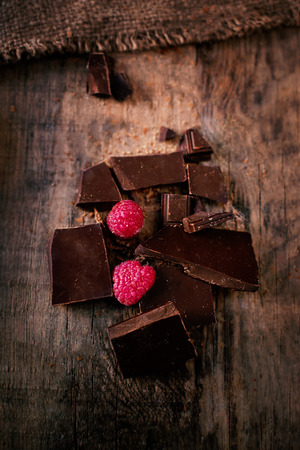 Broken chocolate bar with red ripe  raspberries on dark brown  background close up, macroの写真素材