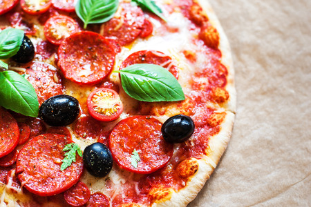 Pepperoni pizza with fresh ingredients on brown baking paper background, top view. Banner or wallpaper の写真素材