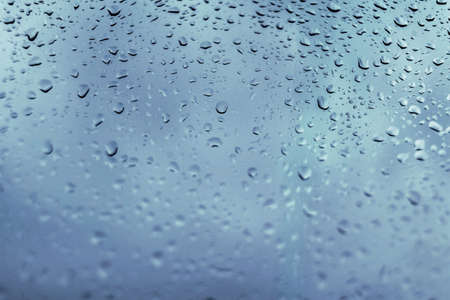 Drops of rain on a blue window glass. Close up   detail of a wet surface water with copy space