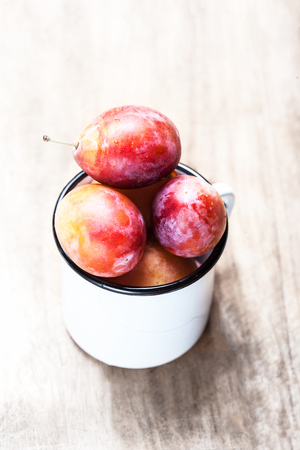 Ripe Pink Plums on white  wood texture background. Fresh plumps on rustic wooden table with copy spaceの写真素材