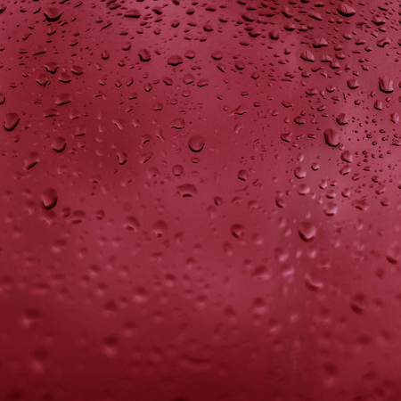 Drops of rain on red glass background. Natural Pattern of raindrops. Rain in the cityの写真素材