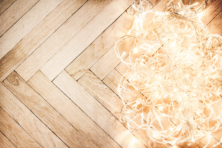 Christmas glowing  lights garland on a old antique wooden parquet floor, sparkling  garland. Christmas background with festive decorationの写真素材