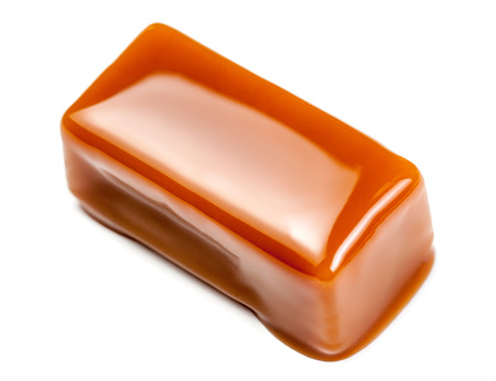 Caramel sauce flowing on caramel candies, isolated on white background. Golden Butterscotch toffee caramel liquid の写真素材