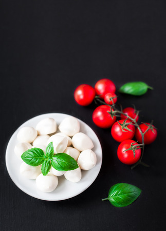 Fresh cherry tomatoes, basil leaf, mozzarella cheese on black slate stone chalkboard with copyspace. Healthy Italian traditional caprese salad ingredients. Organic Mediterranean food concept, flat layの写真素材