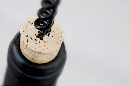 Opening a bottle or red wine with black corkscrew over bright grey blurred background with copespace. Wine degustation concept の写真素材