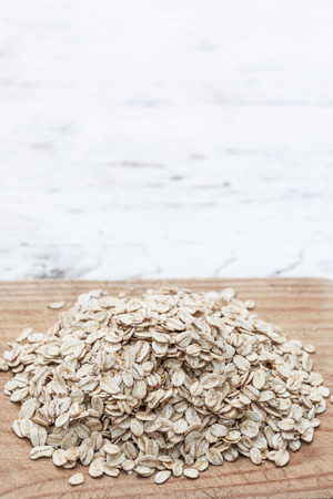 Oatmeal or oat flakes on wood board.   Granola, cereals or rolled oats  on white wooden old table. Healthy breakfast, copy spaceの写真素材