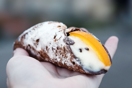 Cannoli on a hand with blurry background. Italian pastries of the Sicily region. Sicilian  cuisine.  Traditional italian dessert with ricotta cheeseの写真素材