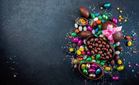 Chocolate easter eggs and sweet candies on dark stone background with copy space. Happy Easter!