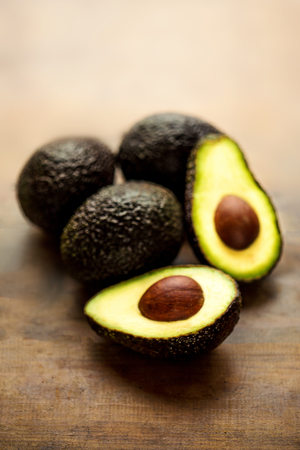 Avocado on a dark wood background. Half and whole avocadoes close up. Top view. Copy space
