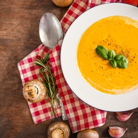 Cream soup with  Pumpkin and Carrot  on Red classic Checkered tablecloth on wooden rustic table. Squash Soup with herbs. Top view. Copy space
の写真素材