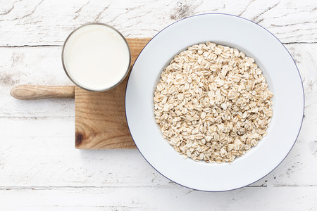 Oatmeal, rolled oats on white wooden background wilt glass of milk. Porridge oats, used in granola...