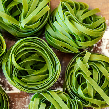 Egg Spinach Pasta Nest on wooden  background, top view. Dry Pasta close up. Italian food concept
