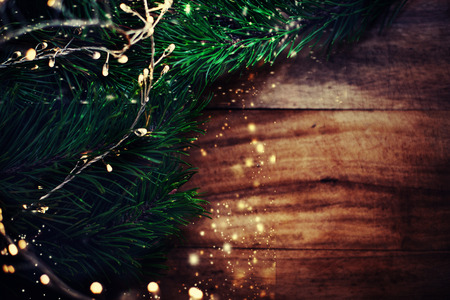 Abstract Golden garland lights and fir tree on  dark wooden  board. Christmas decorations, copyspace. Top viewの写真素材