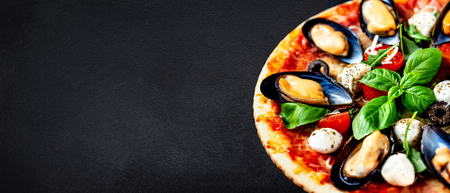 Seafood Italian Pizza on black stone background, top view. Pizza with Mussels, Tomatoes, Basil leaf and Mozzarella Cheese close up. Copy spaceの写真素材