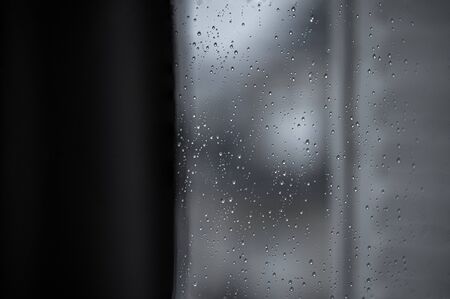 Rain water drops on a black dramatic window glass. Autumn  bokeh depression background. Rain patternの写真素材