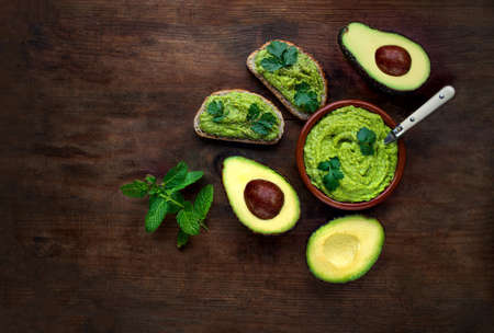 Avocado on dark wooden Background. Guacamole sauce with avocado toast, mint and herbs. Top view. Copy spaceの写真素材