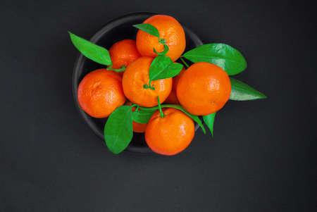 Fresh mandarin oranges fruits or tangerines (clementine) with leaves on dark background. Christmas...