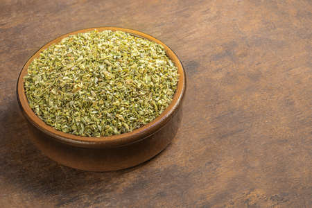 Dried oregano spice on a wooden background. Heap of oregano in a clay bowl. Copyspaceの写真素材