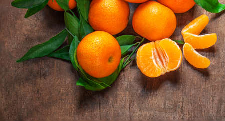 Sweet Mandarines oranges fruits or tangerines with green leaves on a wooden table. Copyspace. Fresh picked mandarins Top view.の写真素材