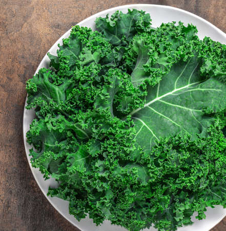 Kale Salad. Fresh Green Kale vegetable leaves on white plate over wooden background, top view. Healthy eating vegetarian food concept.の写真素材