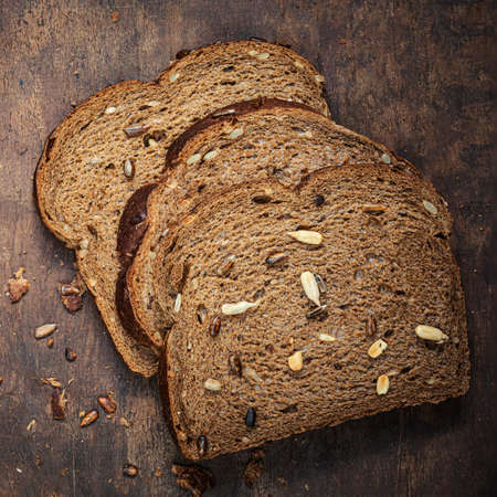 Top view of sliced wholegrain bread on dark ructic wooden background closeup. Freshly baked sourdough bread with seeds and crumbs.の写真素材