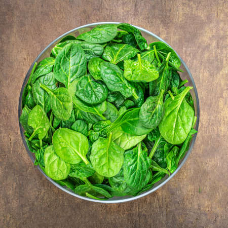 Bowl of Spinach leaves on wooden table. Fresh Spinach Closeup. top view.の写真素材
