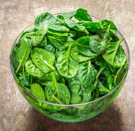 Spinach leaves in a bowl on wooden table. Fresh Spinach Closeup.の写真素材