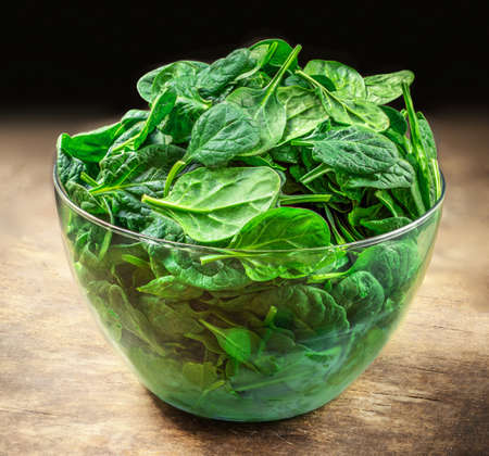 Spinach leaves in a bowl on wooden table. Fresh Spinach Closeup.の写真素材