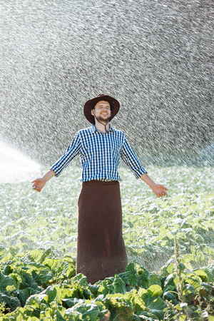 The farmer in the hat is enjoying the rain. Young man getting wet under the rain in summer.の写真素材