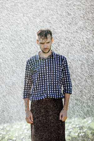 Portrait of a strong, drenched man in the rain. Young man getting wet under the rain in summer.の写真素材