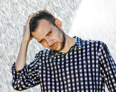 Portrait of a strong, drenched man in the rain. Young man getting wet under the rain in summer.の写真素材