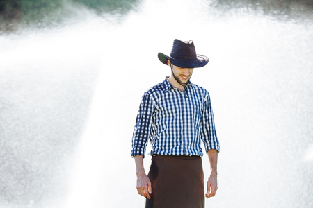 The farmer in the hat is enjoying the rain. Young man getting wet under the rain in summer.の写真素材