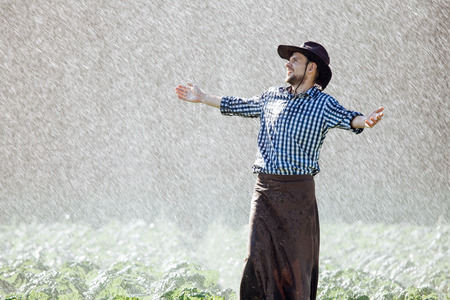 The farmer in the hat is enjoying the rain. Young man getting wet under the rain in summer.の写真素材