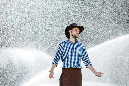 The farmer in the hat is enjoying the rain. Young man getting wet under the rain in summer.の写真素材
