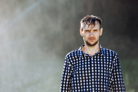 Portrait of a strong, drenched man in the rain. Young man getting wet under the rain in summer.の写真素材
