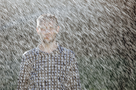 Portrait of a strong, drenched man in the rain. Young man getting wet under the rain in summer.の写真素材