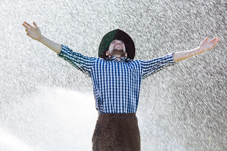 The farmer in the hat is enjoying the rain. Young man getting wet under the rain in summer.の写真素材