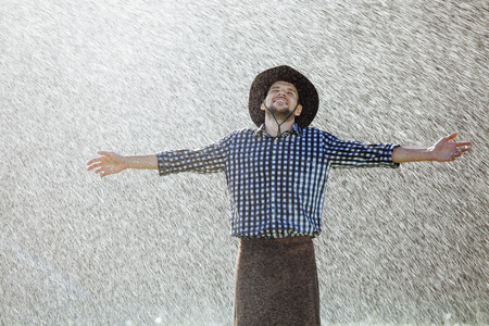The farmer in the hat is enjoying the rain. Young man getting wet under the rain in summer.の写真素材