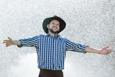 The farmer in the hat is enjoying the rain. Young man getting wet under the rain in summer.の写真素材