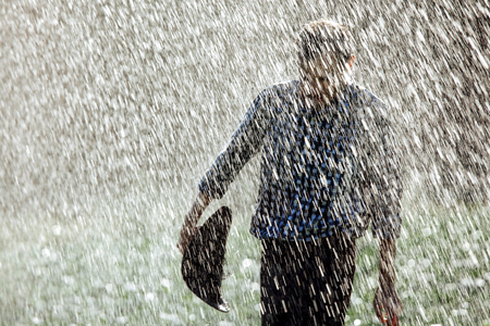 The farmer in the hat is enjoying the rain. Young man getting wet under the rain in summer.の写真素材