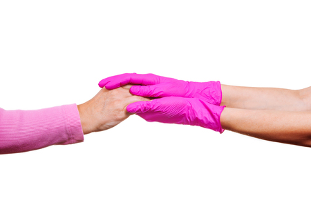 Female hands of a nurse or doctor in pink medical gloves hold hands of an old woman. Concept of care and support in hospice.の写真素材