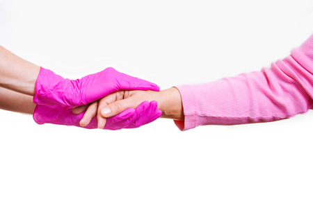 Female hands of a nurse or doctor in pink medical gloves hold hands of an old woman. Concept of care and support in hospice.の写真素材
