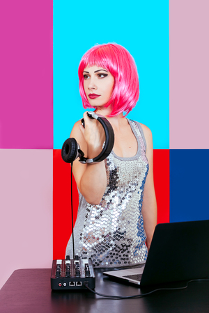 Glamorous DJ girl with pink hair and headphne on red, pink and blue background plays music disko.の写真素材